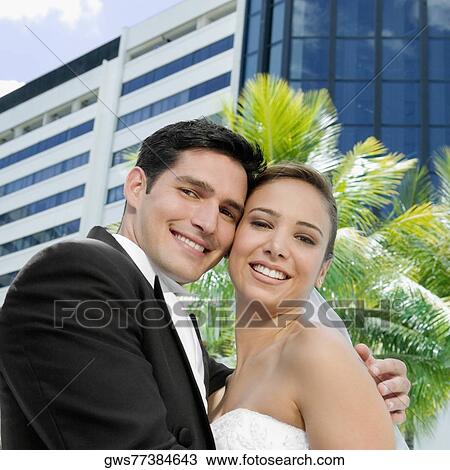 Stock Image - Low angle view of a newlywed couple embracing each other. Fotosearch