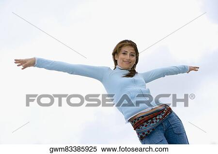 Stock Photography - Low angle view of a young woman standing with her arms outstretched. Fotosearch