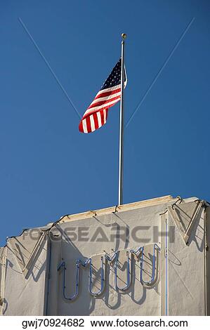 Stock Image - Low angle view of an American flag fluttering on top of a building. Fotosearch