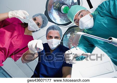 Low angle view of two male surgeons and a female surgeon holding surgical equipments View Large Photo Image Stock Photo - Low angle view of two male surgeons and a female surgeon holding surgical equipments. Fotosearch
