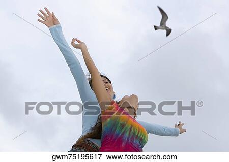 Stock Photo - Low angle view of two women standing with their arms outstretched. Fotosearch