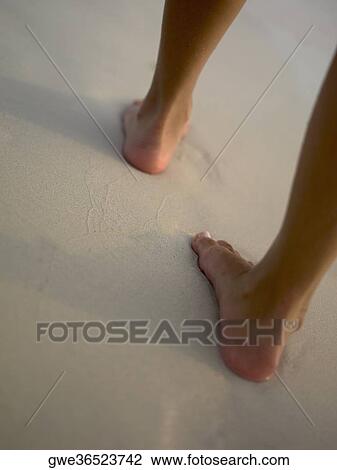 Stock Image - Low section view of a woman walking on the beach. Fotosearch