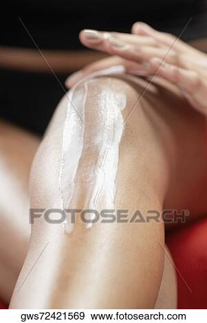 Stock Photo - Low section view of a young woman applying moisturizer on her knee. Fotosearch