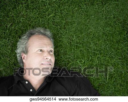 Picture - Mature man lying on the grass in a park. Fotosearch