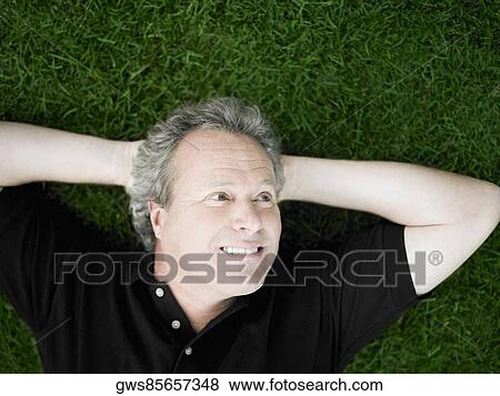 Stock Photo - Mature man lying on the grass in a park. Fotosearch