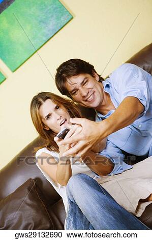 Mid adult couple sitting on a couch and operating a remote control View Large Photo Image Stock Image - Mid adult couple sitting on a couch and operating a remote control. Fotosearch