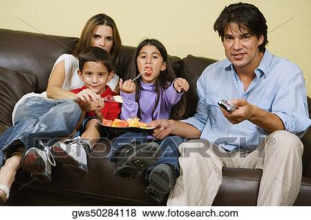 Mid adult couple with their children sitting on a couch and watching television View Large Photo Image Stock Photo - Mid adult couple with their children sitting on a couch and watching television. Fotosearch