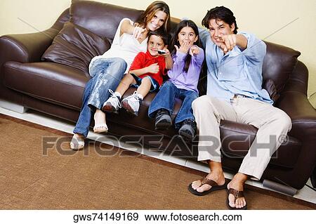 Mid adult couple with their children sitting on a couch and watching television View Large Photo Image Stock Photo - Mid adult couple with their children sitting on a couch and watching television. Fotosearch