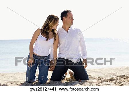 Mid adult man and a young woman kneeling with holding hands on the beach View Large Photo Image Stock Image - Mid adult man and a young woman kneeling with holding hands on the beach. Fotosearch