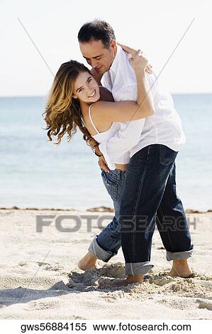 Stock Photography - Mid adult man embracing a young woman on the beach. Fotosearch