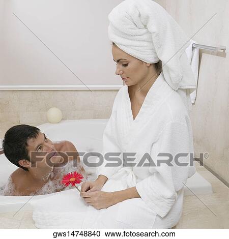 Stock Image - Mid adult man looking at a young woman sitting near him in the bathtub . Fotosearch