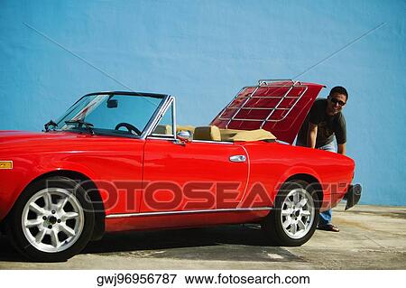 Stock Photo - Mid adult man standing behind a convertible car, Miami, Florida, USA. Fotosearch