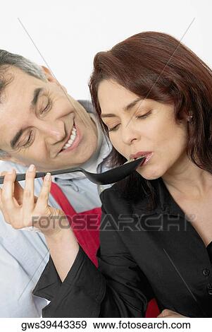 Mid adult woman tasting food with a spoon with a mid adult man looking at her View Large Photo Image Stock Photo - Mid adult woman tasting food with a spoon with a mid adult man looking at her. Fotosearch