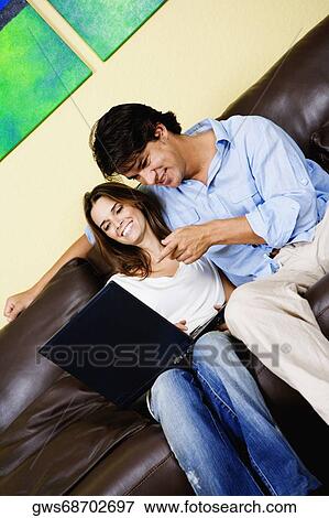 Stock Photo - Mid adult woman using a laptop with a mid adult man sitting beside her. Fotosearch