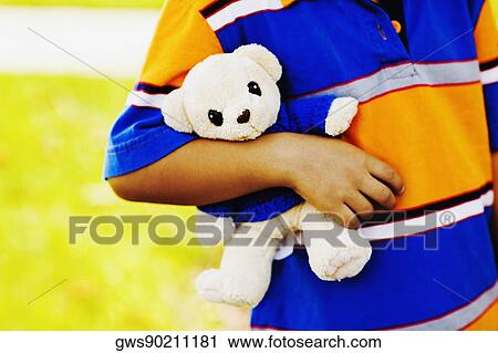 Stock Image - Mid section view of a boy holding a teddy bear. Fotosearch