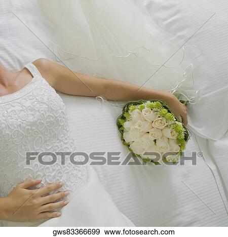 Mid section view of a bride lying on the bed and holding a bouquet of flowers View Large Photo Image Stock Photo - Mid section view of a bride lying on the bed and holding a bouquet of flowers. Fotosearch