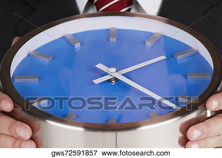 Mid section view of a businessman holding a clock View Large Photo Image Stock Photo - Mid section view of a businessman holding a clock. Fotosearch