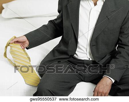 Mid section view of a businessman sitting on the edge of the bed and holding a tie View Large Photo Image Stock Photo - Mid section view of a businessman sitting on the edge of the bed and holding a tie. Fotosearch