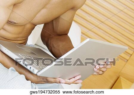Mid section view of a man holding a laptop View Large Photo Image Stock Photography - Mid section view of a man holding a laptop. Fotosearch