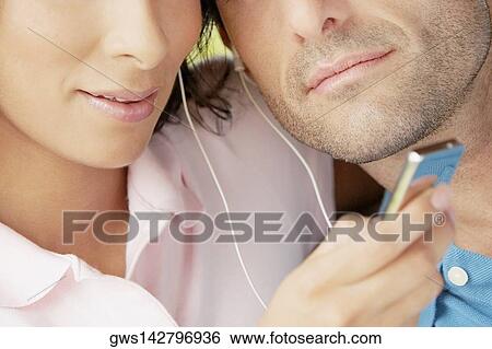 Mid section view of a mid adult couple listening an MP3 player View Large Photo Image Stock Photograph - Mid section view of a mid adult couple listening an MP3 player. Fotosearch