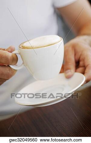 Stock Image - Mid section view of a person holding a coffee cup. Fotosearch