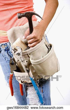 Stock Image - Mid section view of a person holding a hammer in a tool belt. Fotosearch