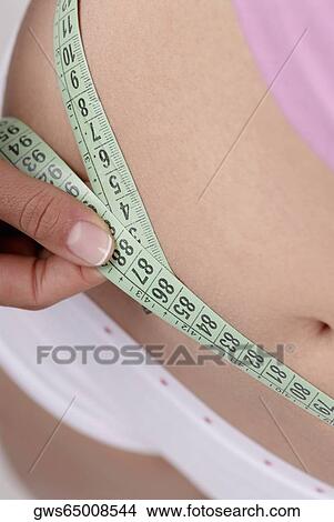 Mid section view of a young woman measuring her abdomen View Large Photo Image Picture - Mid section view of a young woman measuring her abdomen. Fotosearch