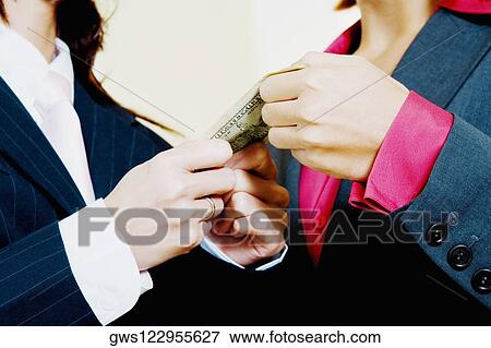 Mid section view of two businesswomen holding a paper currency note View Large Photo Image Stock Photo - Mid section view of two businesswomen holding a paper currency note. Fotosearch