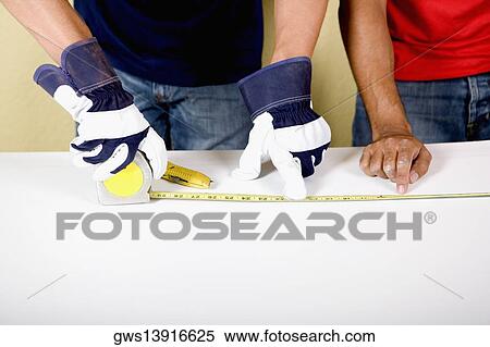Stock Photography - Mid section view of two men measuring with a measuring tape. Fotosearch