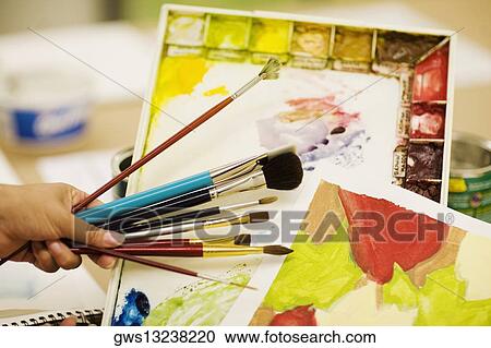 Stock Image - Person's hand holding paint brushes. Fotosearch