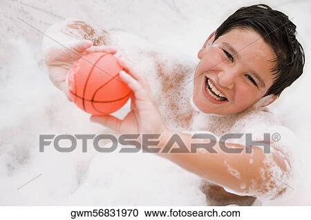 Stock Image - Portrait of a boy holding a ball in a bathtub and smiling. Fotosearch
