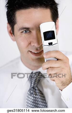 Portrait of a businessman covering his one eye with a mobile phone View Large Photo Image Picture - Portrait of a businessman covering his one eye with a mobile phone. Fotosearch