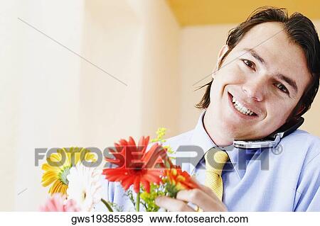 Portrait of a businessman holding flowers and talking on a mobile phone View Large Photo Image Stock Photography - Portrait of a businessman holding flowers and talking on a mobile phone. Fotosearch