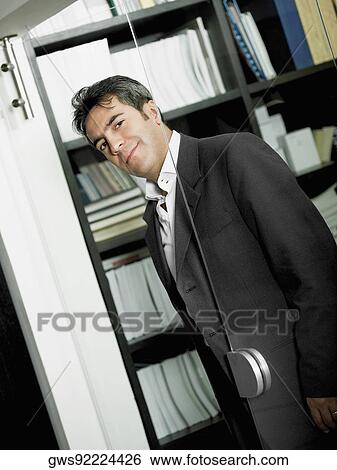 Stock Photograph - Portrait of a businessman looking through a glass door. Fotosearch