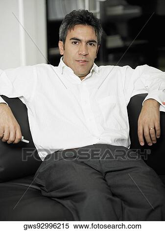 Portrait of a businessman sitting on the couch and holding a mobile phone View Large Photo Image Stock Photography - Portrait of a businessman sitting on the couch and holding a mobile phone. Fotosearch