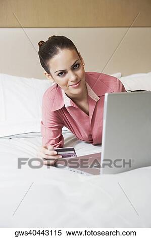 Portrait of a businesswoman holding a credit card and lying in front of a laptop on the bed View Large Photo Image Stock Photography - Portrait of a businesswoman holding a credit card and lying in front of a laptop on the bed. Fotosearch