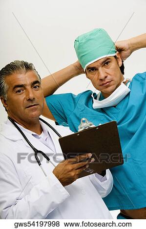 Stock Photo - Portrait of a male doctor holding a clipboard with a male surgeon tying his surgical cap beside him. Fotosearch