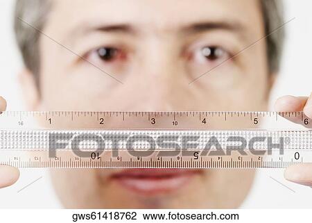 Stock Image - Portrait of a mature man holding a scale in front of his face. Fotosearch