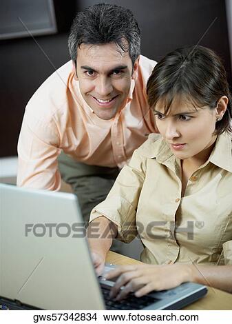 Picture - Portrait of a mature man smiling with a mid adult woman using a laptop beside him. Fotosearch
