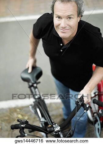 Stock Photograph - Portrait of a mature man standing with a bicycle. Fotosearch