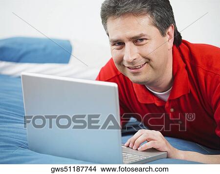 Picture - Portrait of a mature man using a laptop and smiling. Fotosearch