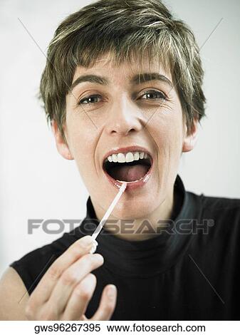 Stock Photography - Portrait of a mature woman applying lipstick on her lips. Fotosearch