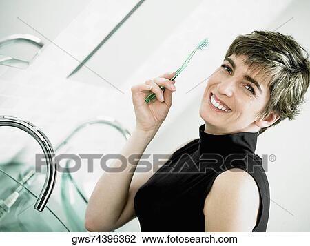 Stock Image - Portrait of a mature woman holding a toothbrush and smiling. Fotosearch