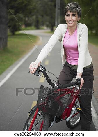 Portrait of a mature woman sitting on a bicycle and smiling View Large Photo Image Stock Photo - Portrait of a mature woman sitting on a bicycle and smiling. Fotosearch