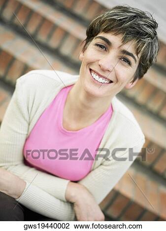 Stock Image - Portrait of a mature woman sitting on steps and smiling. Fotosearch