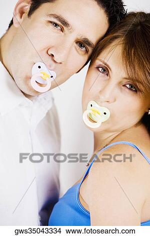 Portrait of a mid adult man and a young woman sucking pacifiers View Large Photo Image Picture - Portrait of a mid adult man and a young woman sucking pacifiers. Fotosearch