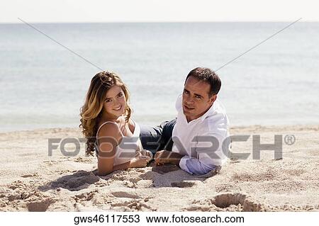 Portrait of a mid adult man and a young woman lying on the beach View Large Photo Image Stock Image - Portrait of a mid adult man and a young woman lying on the beach. Fotosearch