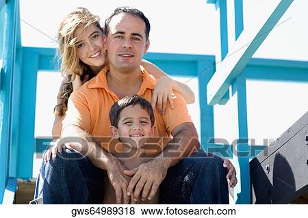 Stock Photo - Portrait of a mid adult man and a young woman sitting with their son in a lifeguard hut. Fotosearch