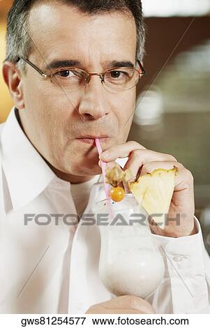 Stock Photo - Portrait of a mid adult man drinking pina colada with a drinking straw. Fotosearch