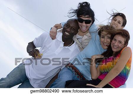 Stock Image - Portrait of a mid adult man holding a glass of juice and smiling with his friends. Fotosearch